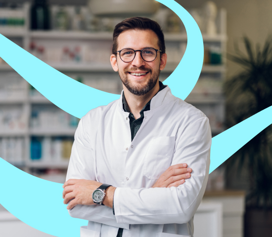 Person wearing a white lab coat and glasses stands with arms crossed in a pharmacy, with shelves of medicines and healthcare products in the background.