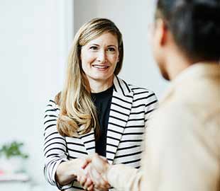 A woman in a smart stripped jacket shaking hands with a man
