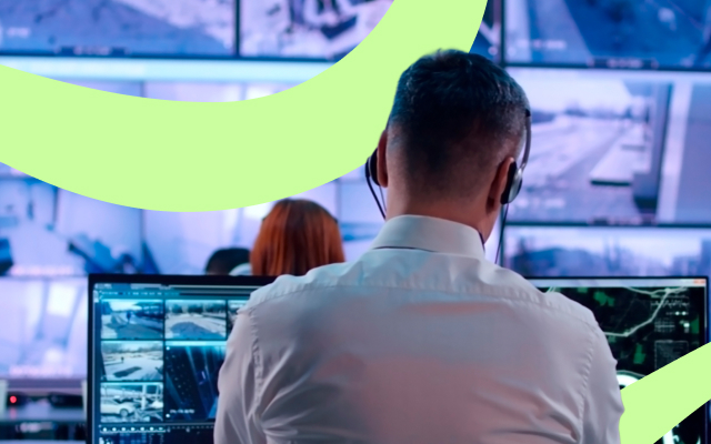 Person in a white shirt and headphones monitoring multiple surveillance screens, with another individual visible in the background.