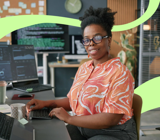 Woman with glasses working at a computer workstation with multiple monitors displaying code in a modern office.