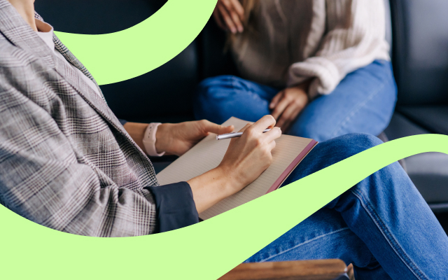 Two people sitting and talking, with one person writing in a notebook.