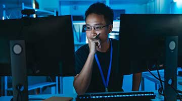 Thoughtful male sitting in front of two monitors