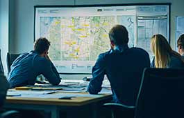 A small group of people in a conference room studying a map on a large screen