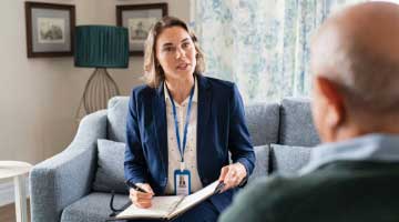 Health professional sitting with a older man in a living room 