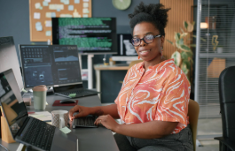 Person with glasses working at a computer desk with code displayed on multiple screens.