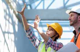 Two construction workers wearing helmets looking up at a roof 