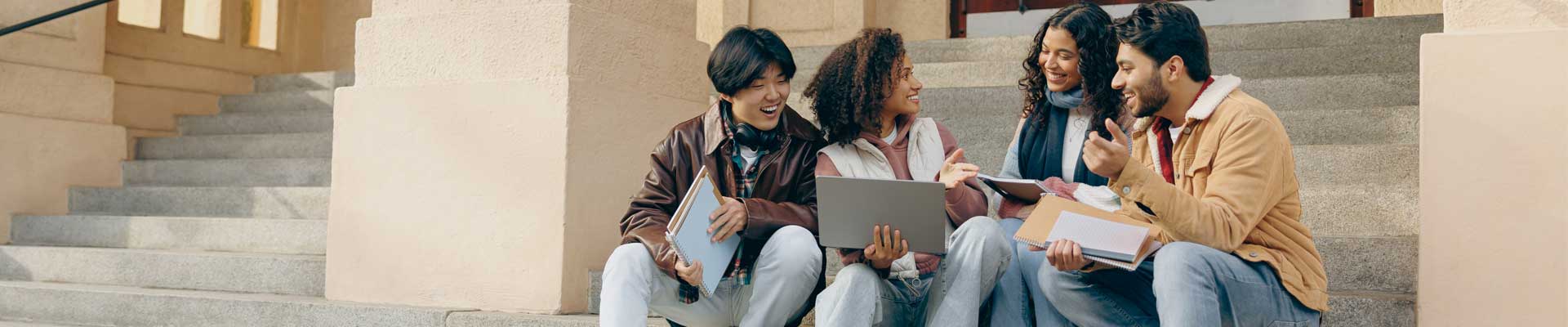 a group of students sat on stairs, smiling with laptops