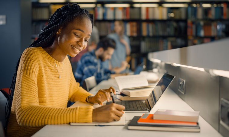 student sat in a library on a laptop