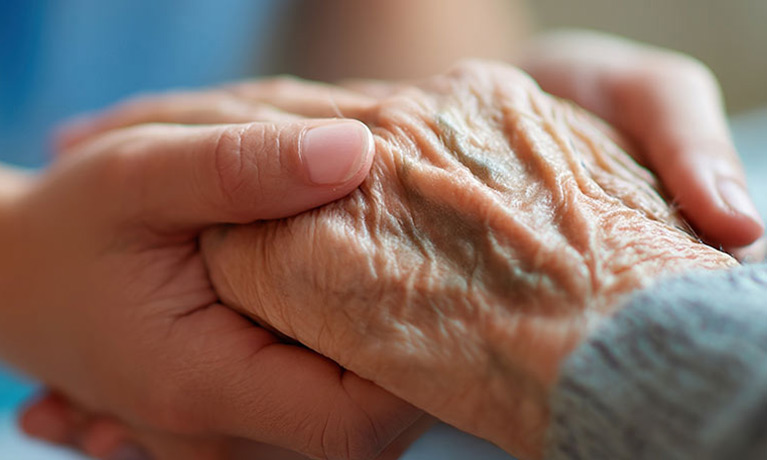 A nurse holding an elderly patients hand