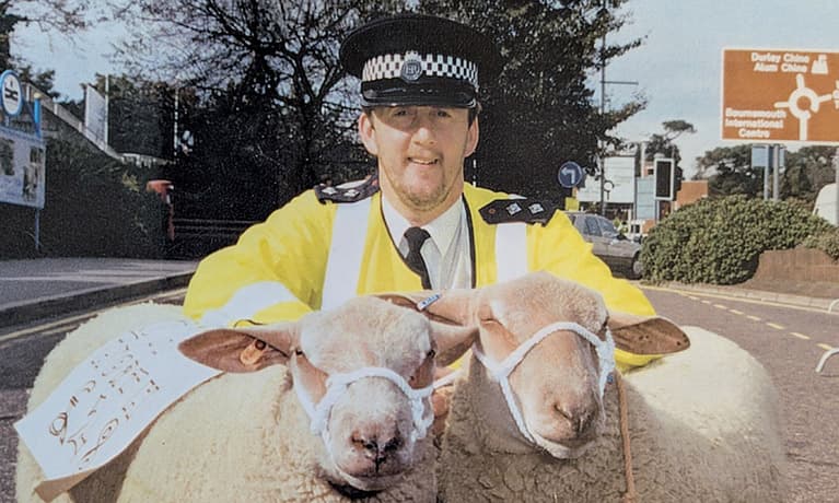 Alan Jenkins stood with two sheep in his police uniform smiling