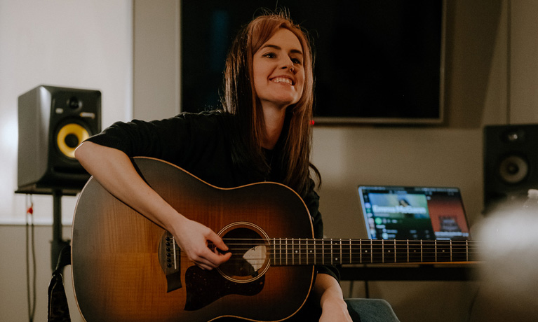 Emma McGann playing guitar in a studio