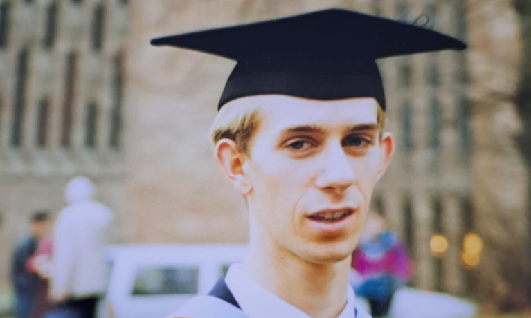 Phil Adcock smiling in a graduation cap