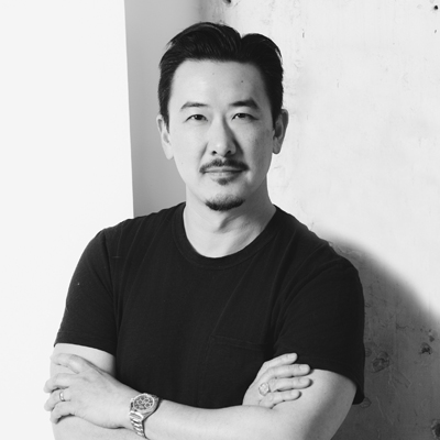 A black and white photo of David Imai looking at the camera with his arms crossed