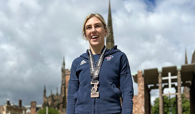 Emma Reid stood smiling in front of Coventry Cathedral, wearing her World Championship medal around her neck