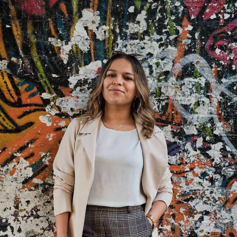 Camila stood against a brick wall covered in street art