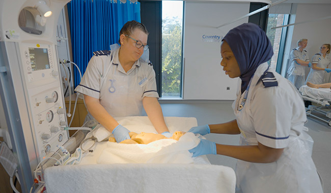 Two midwifery students holding a mannequin baby in a towel