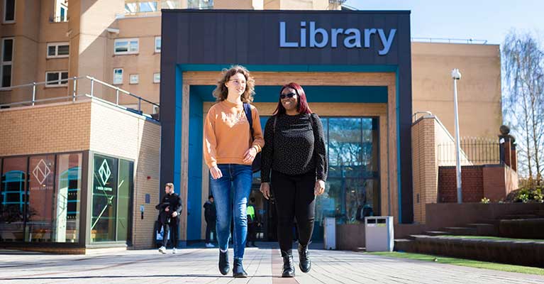 Two female students walking away from the Coventry University library