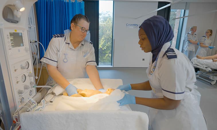 Two midwifery students holding a mannequin baby in a towel