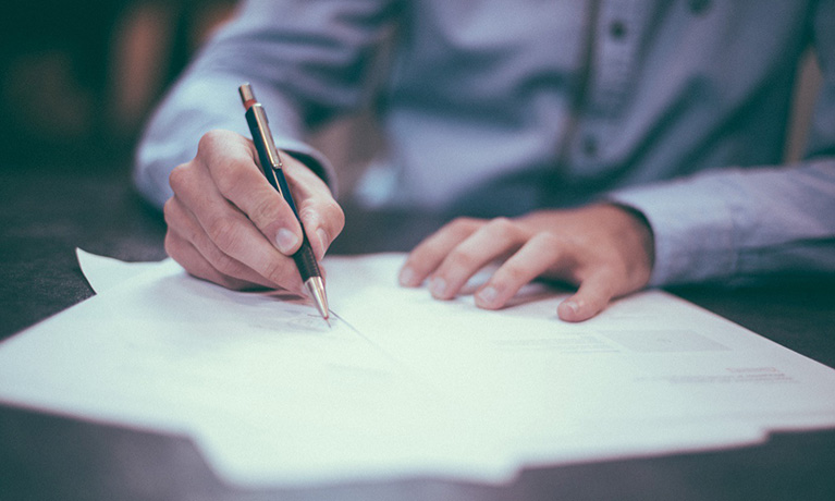 someones hand holding a pen writing on paper wearing a shirt