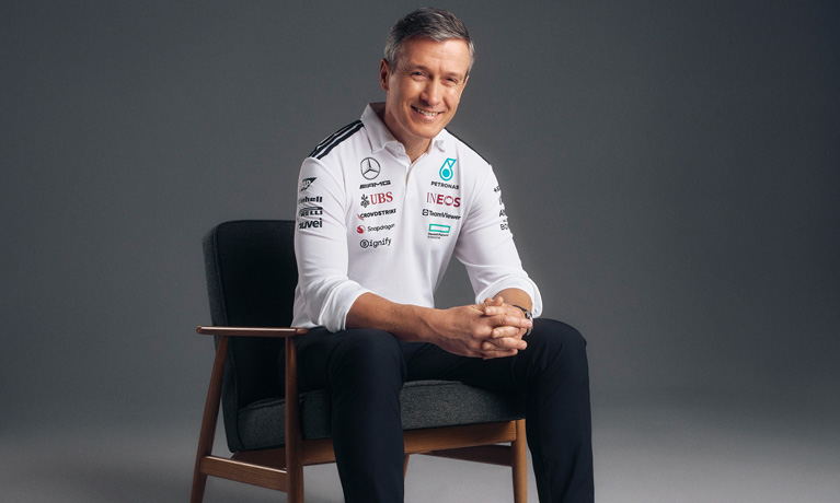 Rob Thomas smiling sat on a chair with a studio plain background