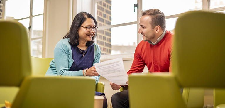 two people chatting in an informal setting looking at a document 