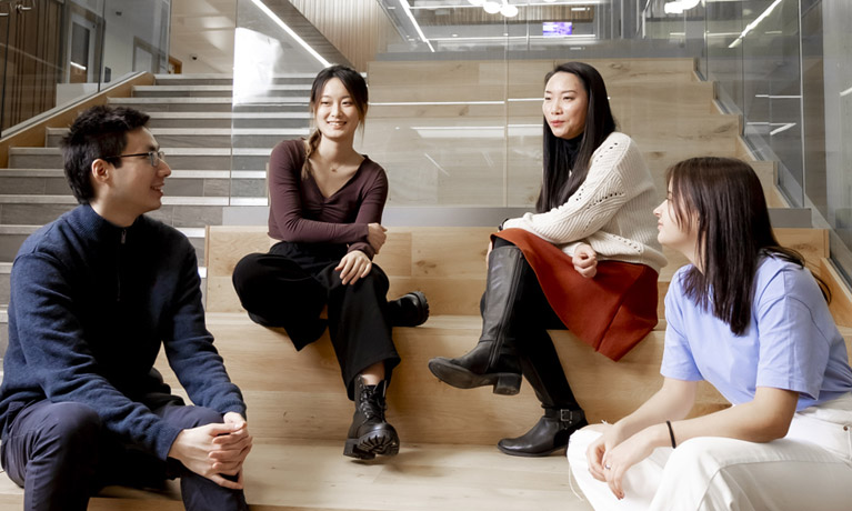 A group of four international students sat chatting in an open study area on campus.study 