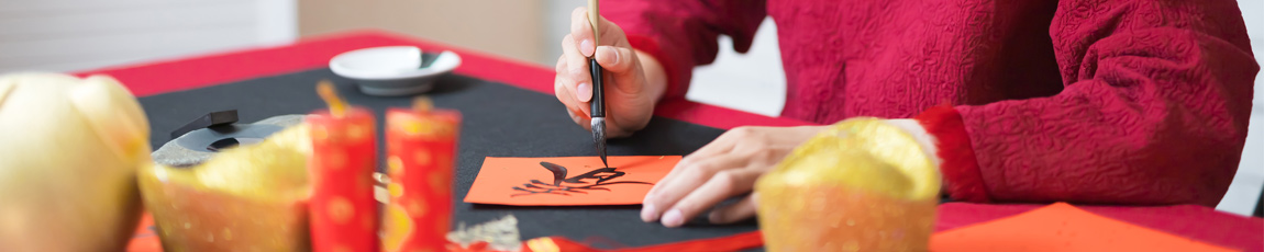 A close up of hands holding a traditional Chinese paintbrush and writing Chinese characters.