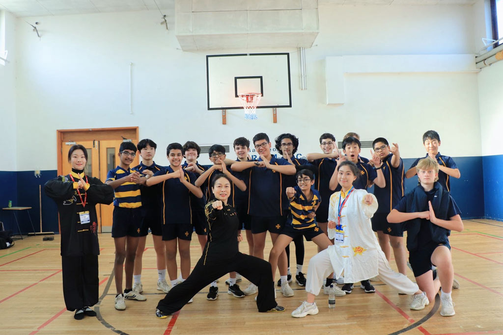 A group of school students in a gym doing martial arts poses and smiling at the camera.