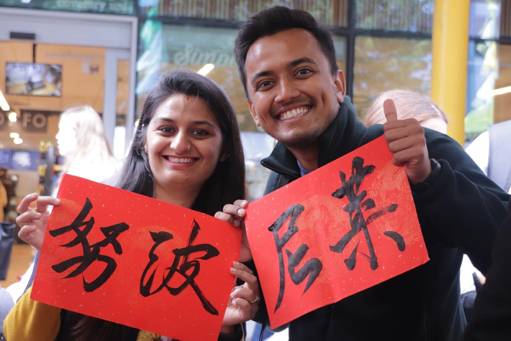 Two people smiling and holding up Chinese calligraphy examples.