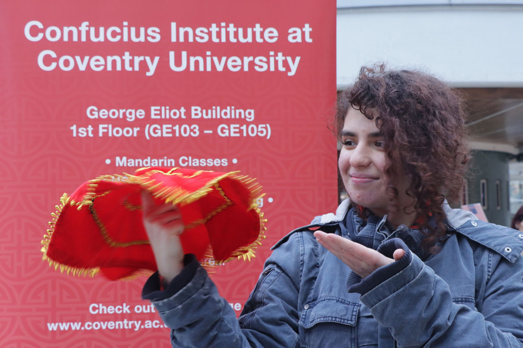 A woman in front of a Confucius Institute with a Chinese fabric hat.