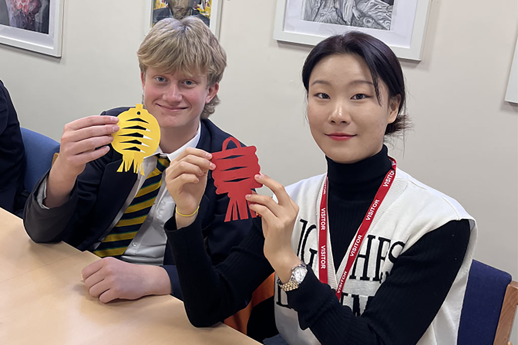 A student and teacher holding up paper cut Chinese decorations.