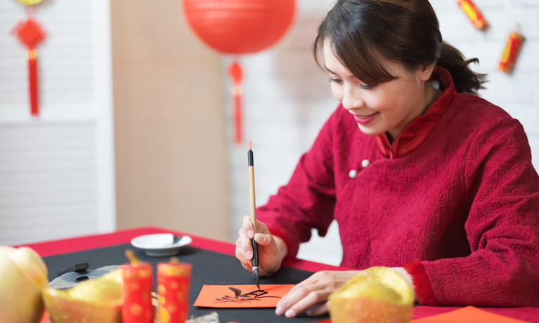 A Chinese woman surrounded by red paper lanterns, writing Chinese caligraphy with a traditional brush and ink.