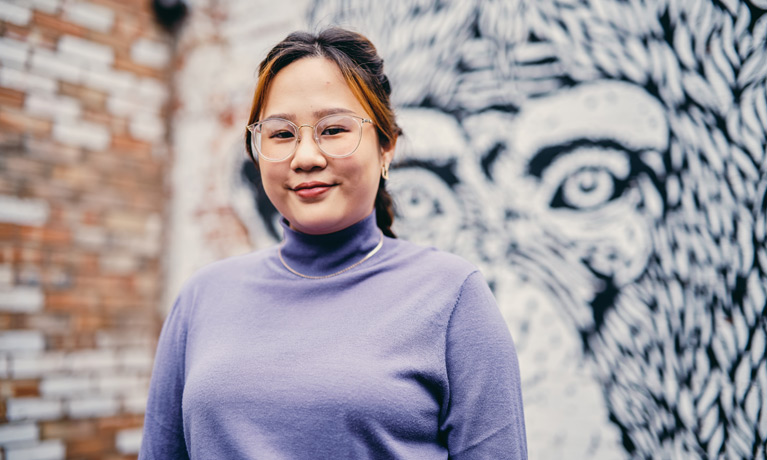 An international student in Fargo Village, against a background of a wall of modern street art.