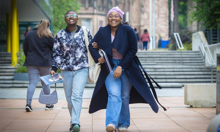 A student and their parent visiting Coventry University at an open day, walking past the Hub with their arms linked.
