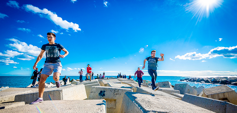 A group of students running along the coast with a blue sky and sea behind them.