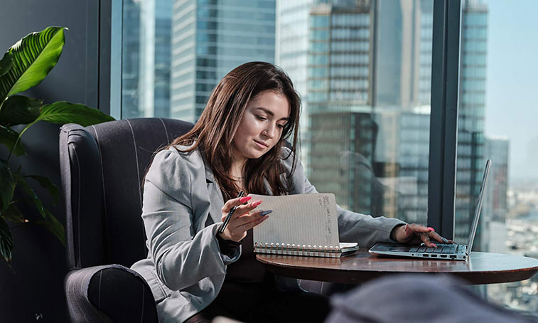professional looking woman looking at a notepad and a laptop