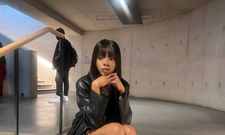 Laura Onome Momodu sitting on a stairwell wearing a leather coat