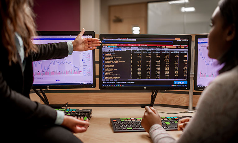 Two people looking at screens displaying stock market stats