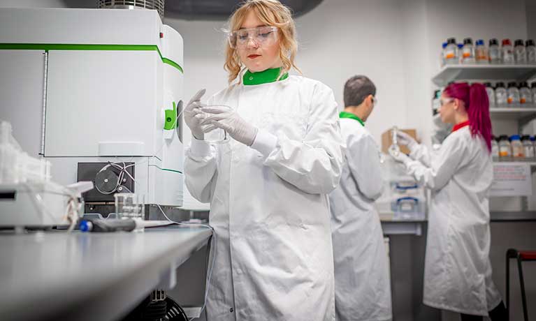 Blonde lady wearing a lab white suite looking into a dish