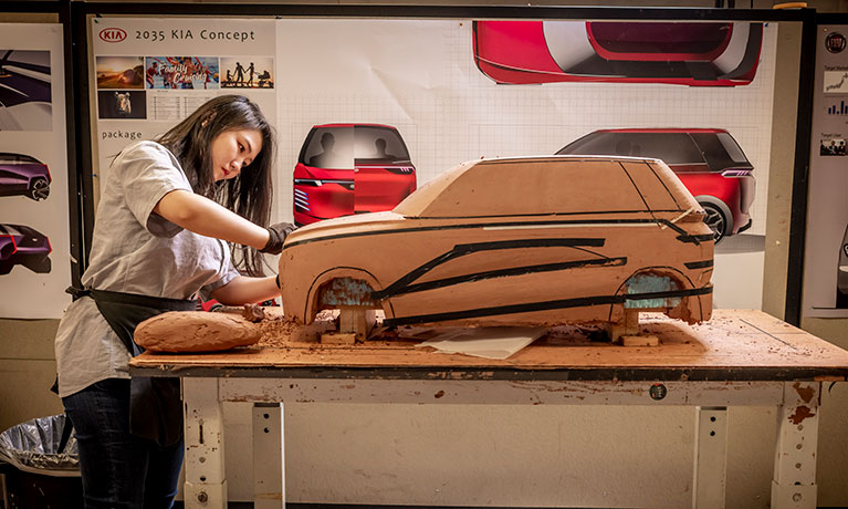 woman in a grey top working on a large clay model of a car to improve the design