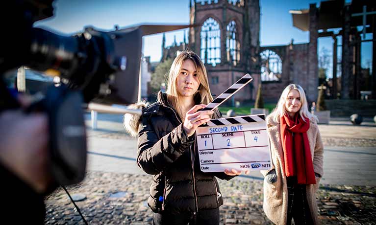 Woman with clipboard stood in front of Coventry Cathedral being filmed