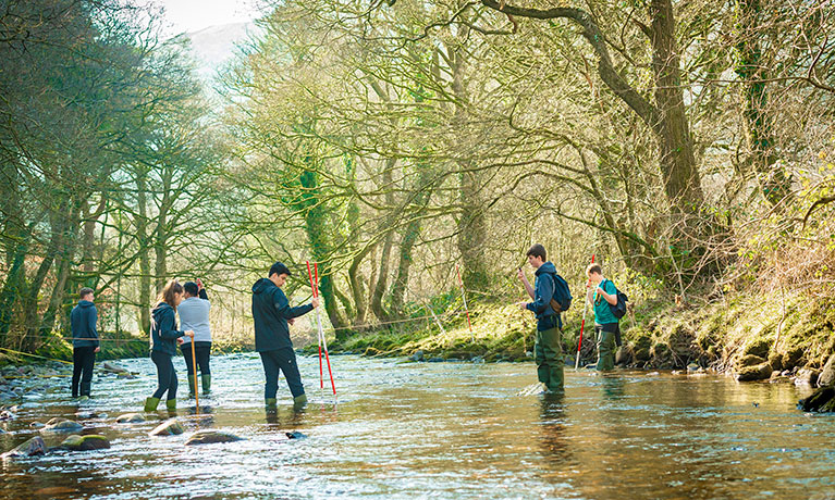 Seven students stood in a river with tools