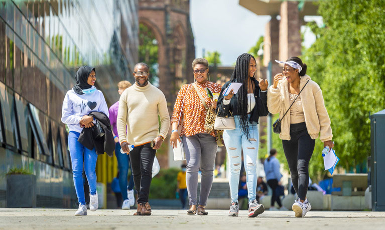 A group of international students walking outside on a sunny day at the Coventry University campus