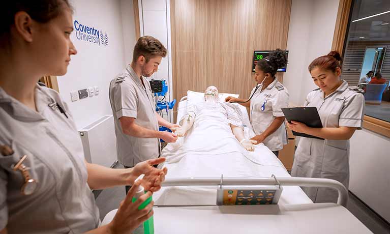 trainee nurses taking notes around a manikin on a hospital bed 