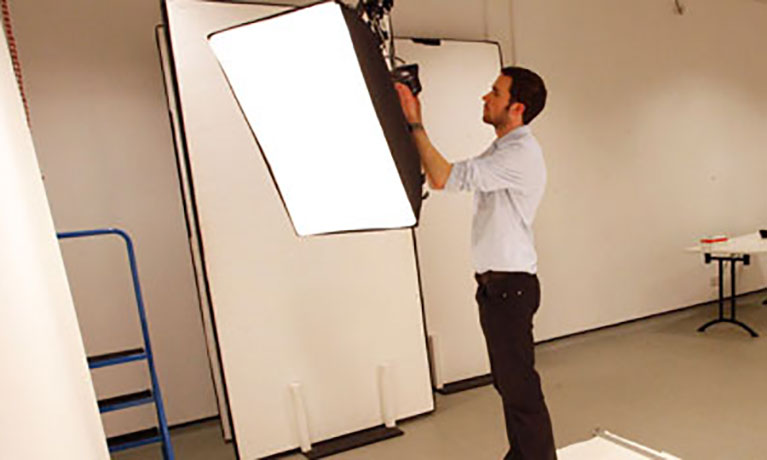 Male student setting up a photography light in a studio.