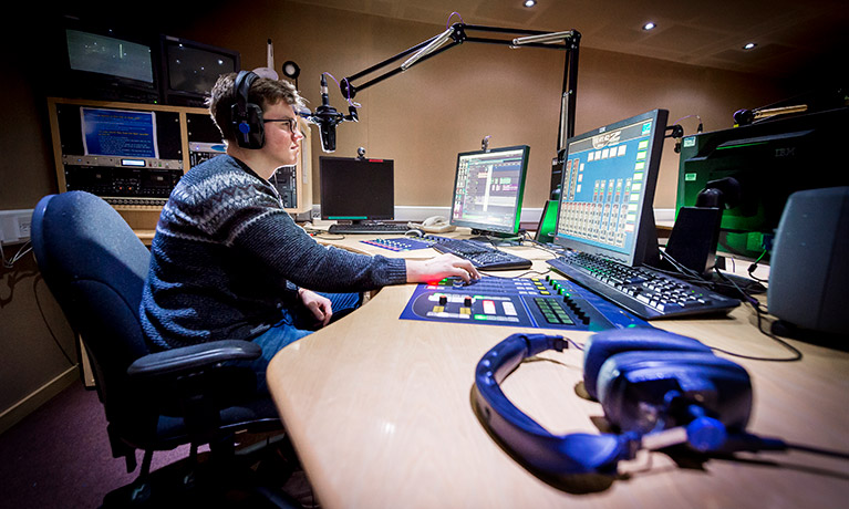 Student using computer equipment on a recording studio desk.