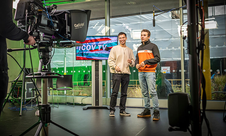 Two male students presenting in a TV studio to a camera in the foreground.