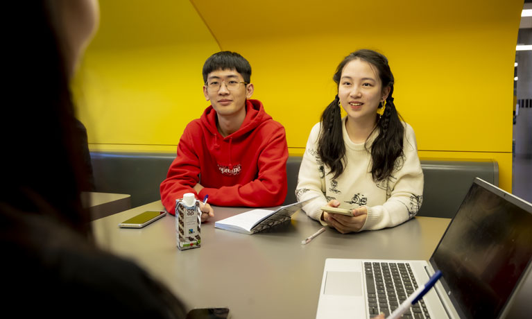Two student sat across a table talking to an individual out of shot