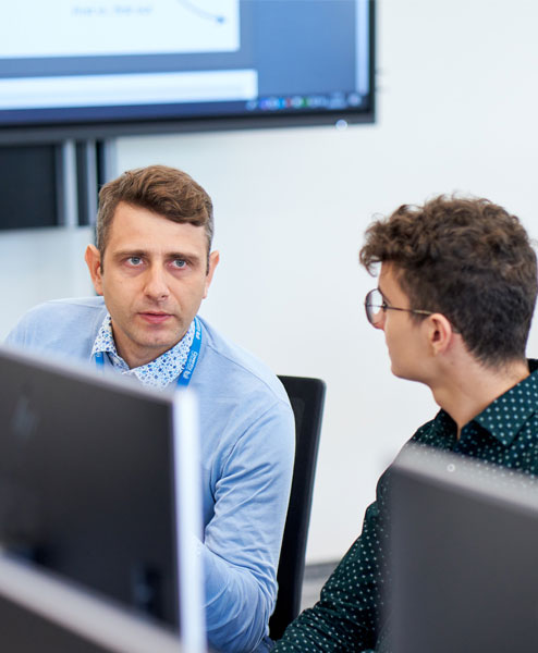 teacher and student sitting at computers conversating