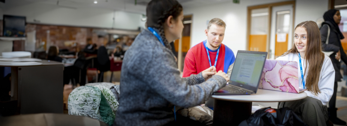 students wearing lanyards sitting around a table with their laptops